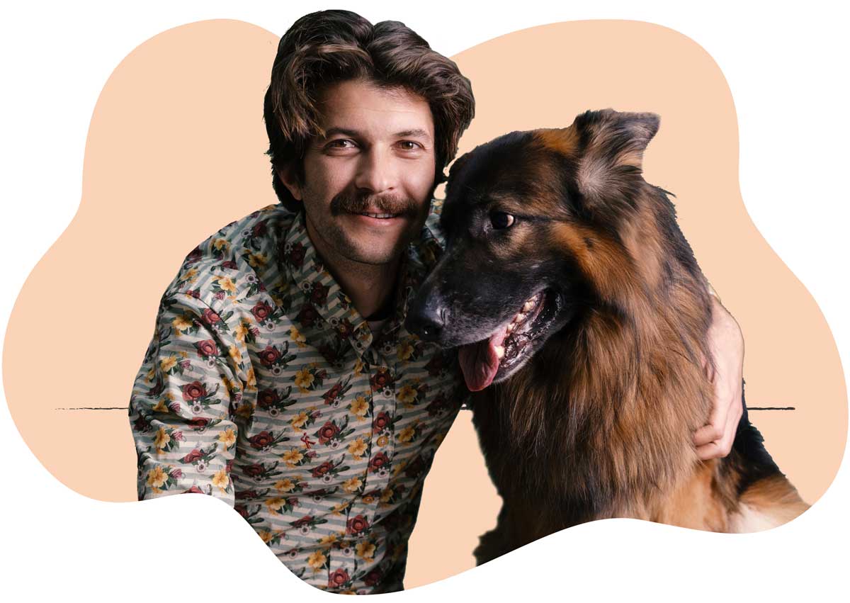 A man in a brown shirt sitting next to his shaggy brown-haired dog