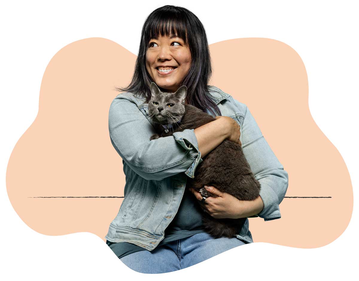 A woman in a denim coat holding her small gray cat in her lap