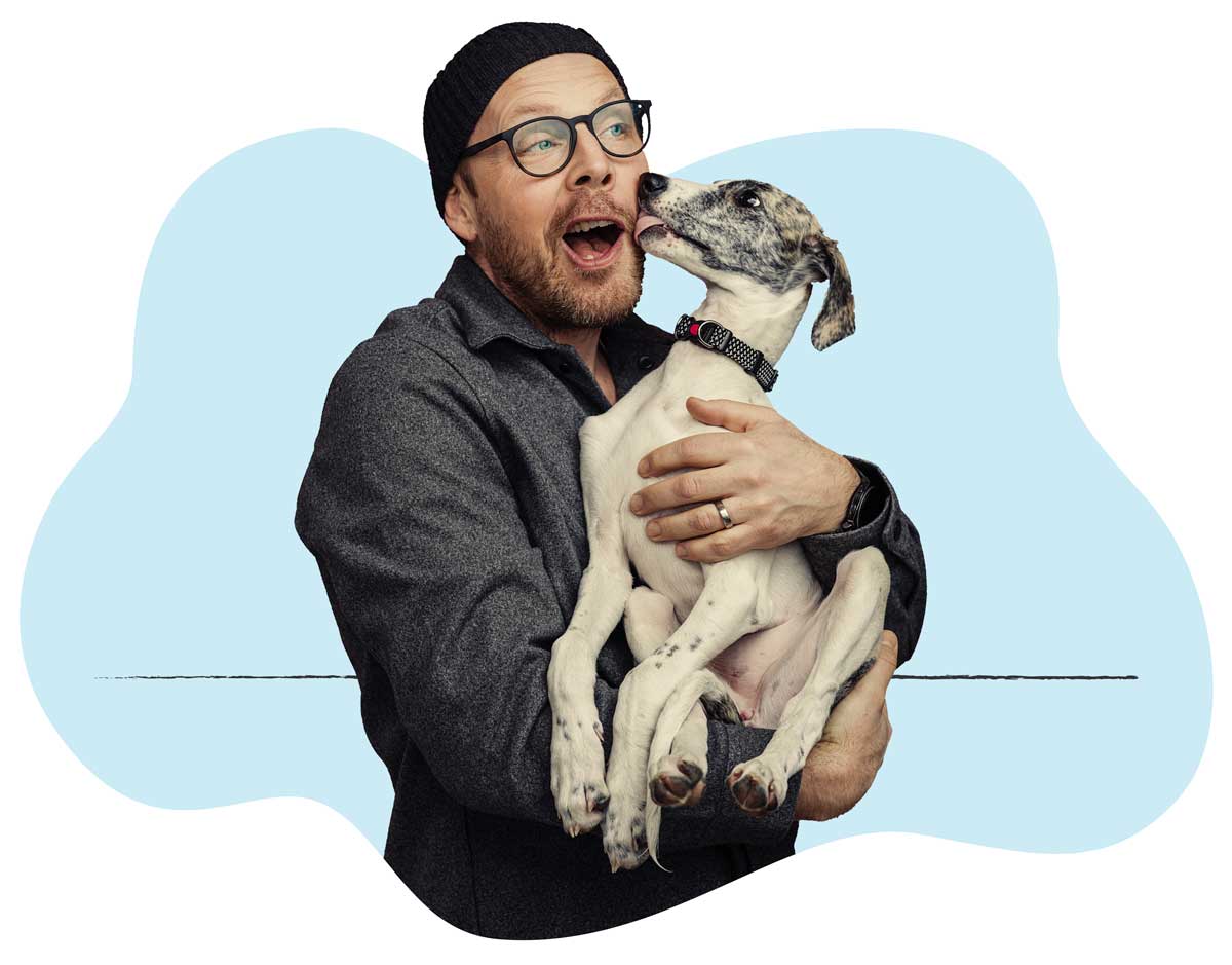 A man in a gray long-sleeve shirt gets a kiss from his dog