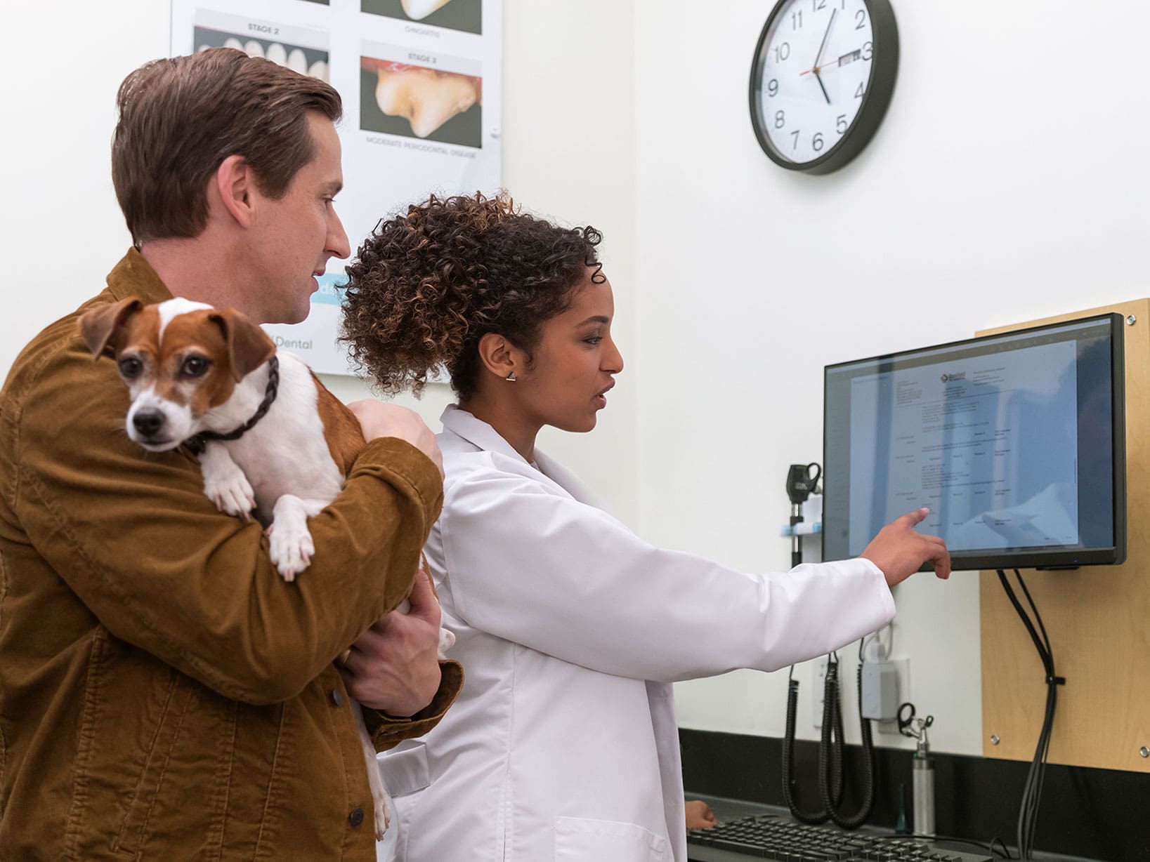 A man holding a small dog next to a vet examining charts