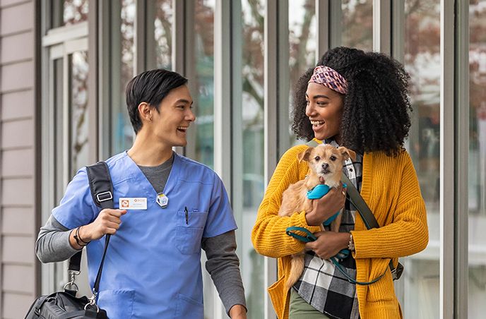 A woman carrying a small dog walking next to a Banfield Associate